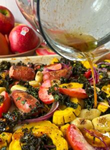 Drizzle of Sage Brown Butter over a sheet pan feel with squash, lucy apples, and kale. a bowl of lucy apples is in the background, as well as one cut open showing the read flesh
